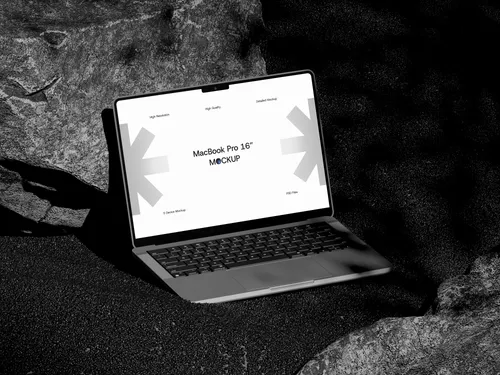 MacBook Pro on sand rock, top front view, open lid, screen glowing.
