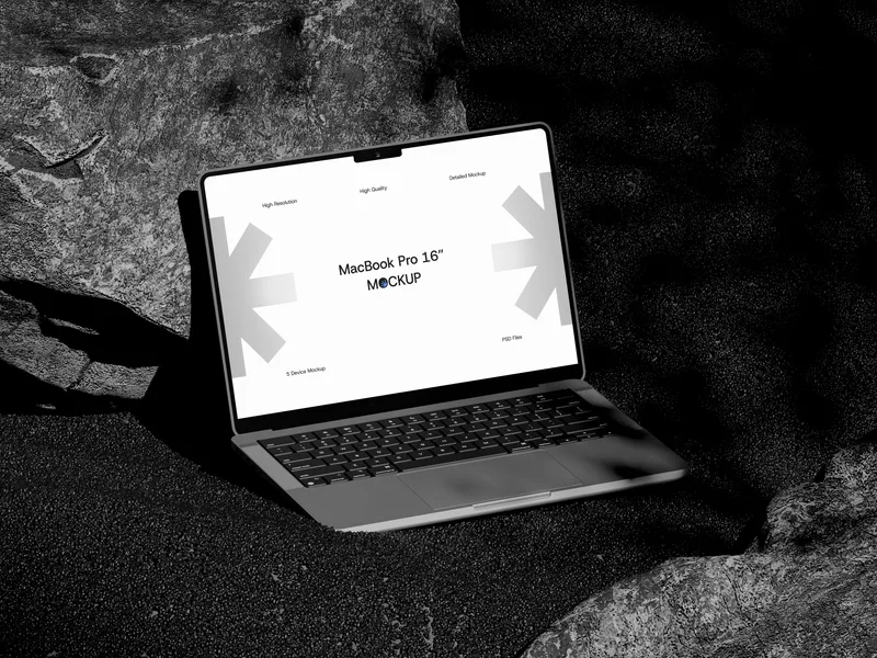 MacBook Pro on sand rock, top front view, open lid, screen glowing.